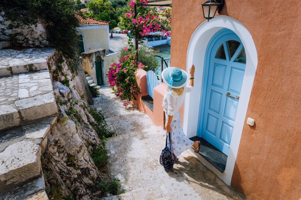 Travel tourist woman on vacation in Greece. Person with blue sunhat in front of traditional