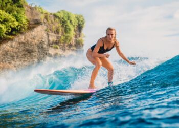 woman surfing in one of the best beaches for water sports (Source: Canva)