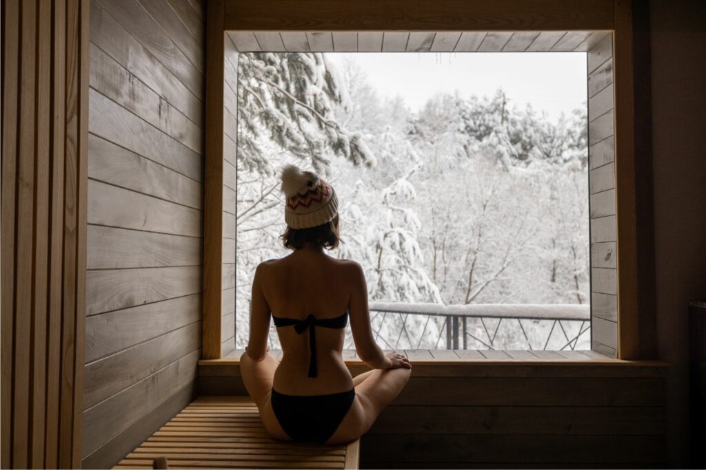Woman admiring winter scenery from sauna at spa resort