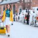 Young Woman On a Solo Road Trip Wearing a Bright Yellow Jacket and Yellow Rolling Suitcase (Source: Canva)