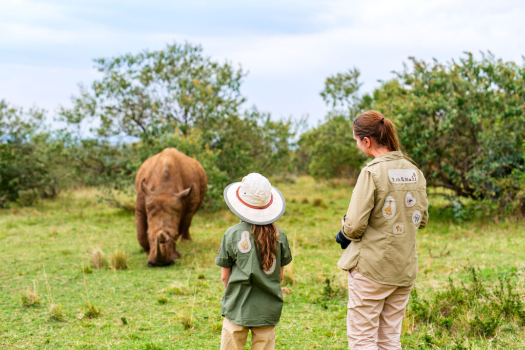 Back view of a mother and daughter on safari walking near a white rhino