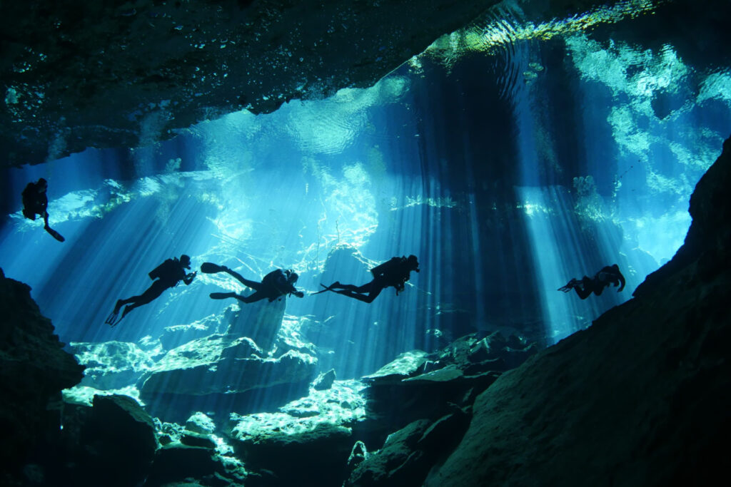 Five divers cave diving in Cenotes, Mexico, the dangerous yucatan, dark cavern landscape underwater