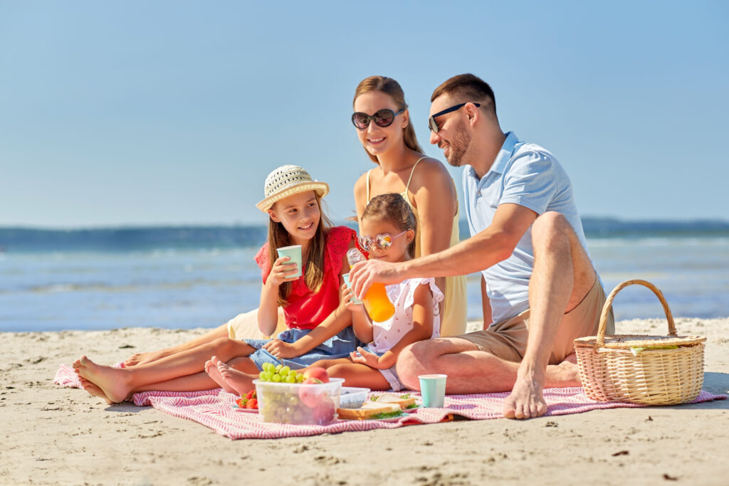 happy family having picnic on summer beach and drinking juice