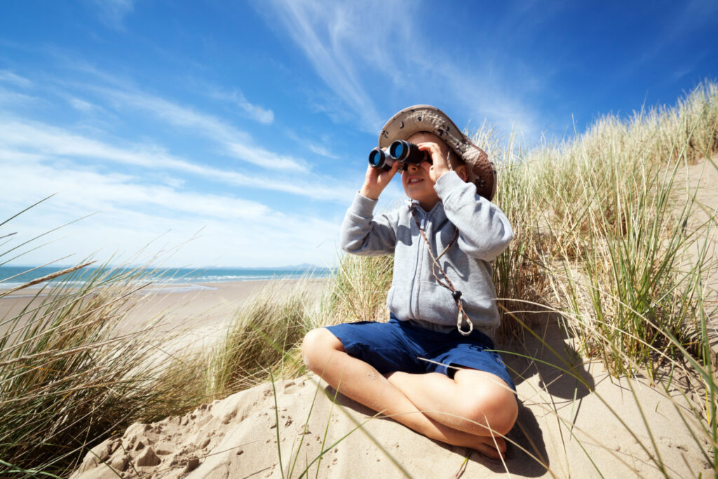 little boy bird watching with binoculars at the beach