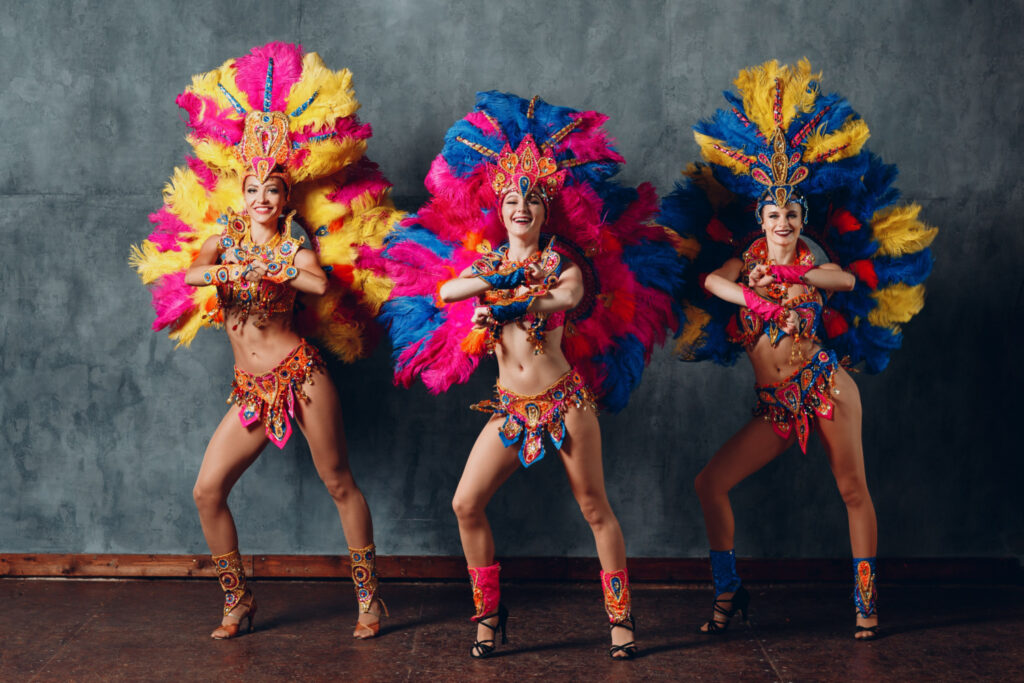 three women dancing in vibrant brazilian samba carnival costumes adorned with colorful feather plumage