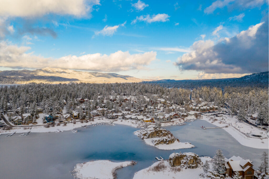 Aerial view of Big Bear Lake with the lake frozen and pine trees below on a sunny blue sky day