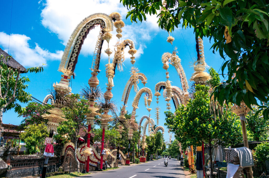 Traditional Balinese penjors along the street of Bali, Indonesia. Tall bamboo poles with decoration are set in honour of Hindu gods on religious festivals like Galungal, Kuningan.  Imagentle/Shutterstock